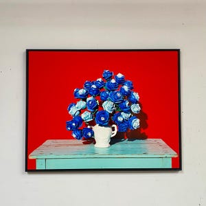 May include: A framed artwork featuring a vibrant display of blue roses in a white vase. The roses sit on a weathered, turquoise table against a bold red backdrop. The piece is a striking floral still life.