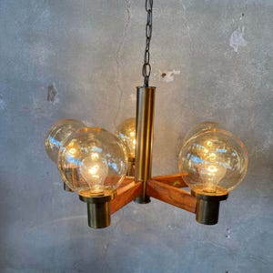 May include: A chandelier featuring a central brass-toned column and four wooden arms extending outward. Each arm supports a spherical glass globe containing a single light bulb. The fixture is suspended by a metal chain from the top center.