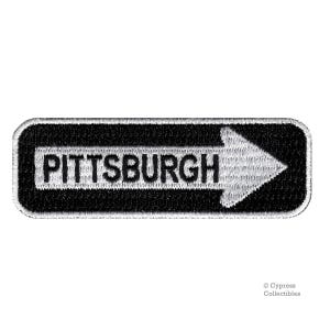 May include: Black and white embroidered patch with a white arrow pointing to the right and the word "PITTSBURGH" in white letters.