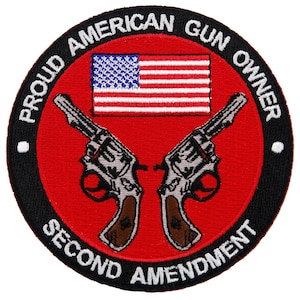 Puede incluir: Un parche bordado en rojo, blanco y azul con el texto "Proud American Gun Owner Second Amendment" alrededor del borde. El centro del parche presenta un par de revólveres plateados cruzados y una bandera estadounidense.