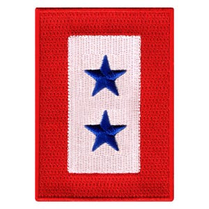May include: A red, white, and blue embroidered patch with two blue stars on a white background. The patch is surrounded by a red border.