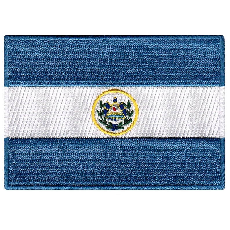 May include: A blue and white embroidered patch with the national flag of El Salvador. The flag features a white horizontal stripe with the national coat of arms in the center, surrounded by a yellow circle.