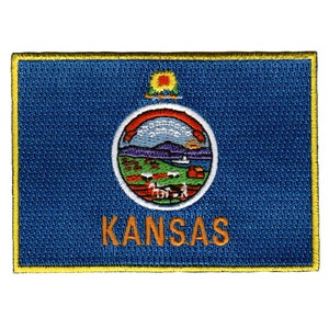 May include: An embroidered patch featuring the state flag of Kansas. The patch is blue with a yellow border and depicts the state seal of Kansas, which includes a sunflower, a river, and a prairie scene. The word "KANSAS" is written in orange below the seal.