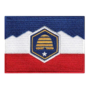 Puede incluir: Un parche bordado con la bandera de Salt Lake City, Utah. La bandera es azul, blanca y roja con un emblema hexagonal en el centro. El emblema presenta una colmena estilizada en oro y una estrella blanca.