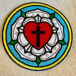 May include: Embroidered patch with a white rose, a red heart with a black cross, and a blue and yellow border.