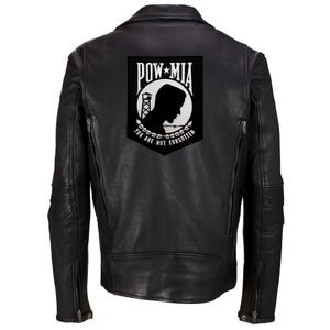 Può includere: Giubbotto di pelle nero con una toppa bianca POW MIA sul retro. La toppa presenta la silhouette di un prigioniero di guerra, una torre di guardia, filo spinato e il testo "You Are Not Forgotten".