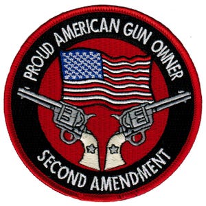 Puede incluir: Un parche bordado en rojo, blanco y azul con un par de pistolas cruzadas, una bandera estadounidense y el texto "Proud American Gun Owner Second Amendment".