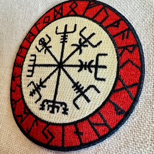 May include: A red and black embroidered patch with a white compass design in the center. The compass has eight points and is surrounded by a circle of runes.