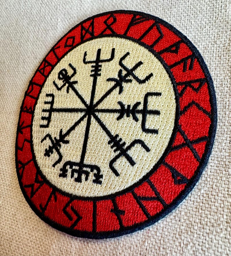 May include: A red and black embroidered patch with a white compass design in the center. The compass has eight points and is surrounded by a circle of runes.
