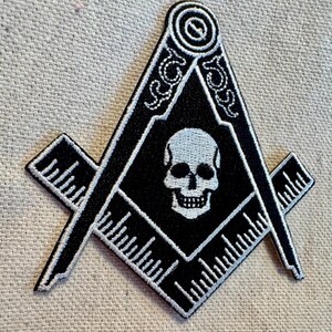 May include: Black and white embroidered patch of a skull inside a square and compass, a symbol of Freemasonry.