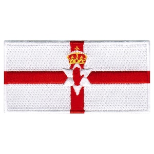 Puede incluir: Una bandera blanca con una cruz roja y una mano roja con una corona en la parte superior. La bandera está bordada con un fondo blanco y costuras rojas.