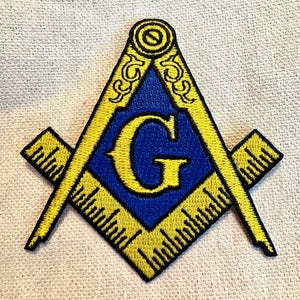 Può includere: Una toppa ricamata con un simbolo massonico, una squadra e un compasso con una 'G' al centro, in giallo e blu.
