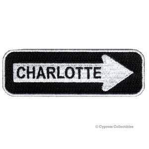 May include: Black and white embroidered patch with a white arrow pointing to the left and the word "CHARLOTTE" in white text.