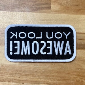 May include: Black and white embroidered patch with the text "YOU LOOK AWESOME!" in white lettering on a black background.