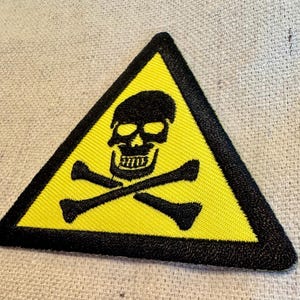 May include: A yellow triangle warning sign with a black skull and crossbones. The sign has a black border.