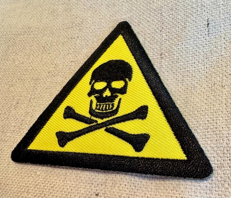 May include: A yellow triangle warning sign with a black skull and crossbones. The sign has a black border.