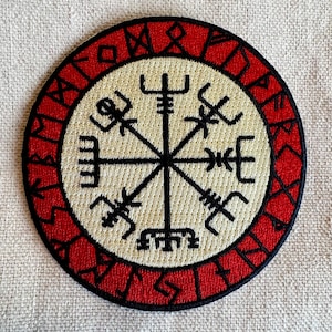 Op de afbeelding: Een rood en wit geborduurde patch met een zwart kompasontwerp. Het kompas heeft acht punten en is omgeven door een cirkel van runen.