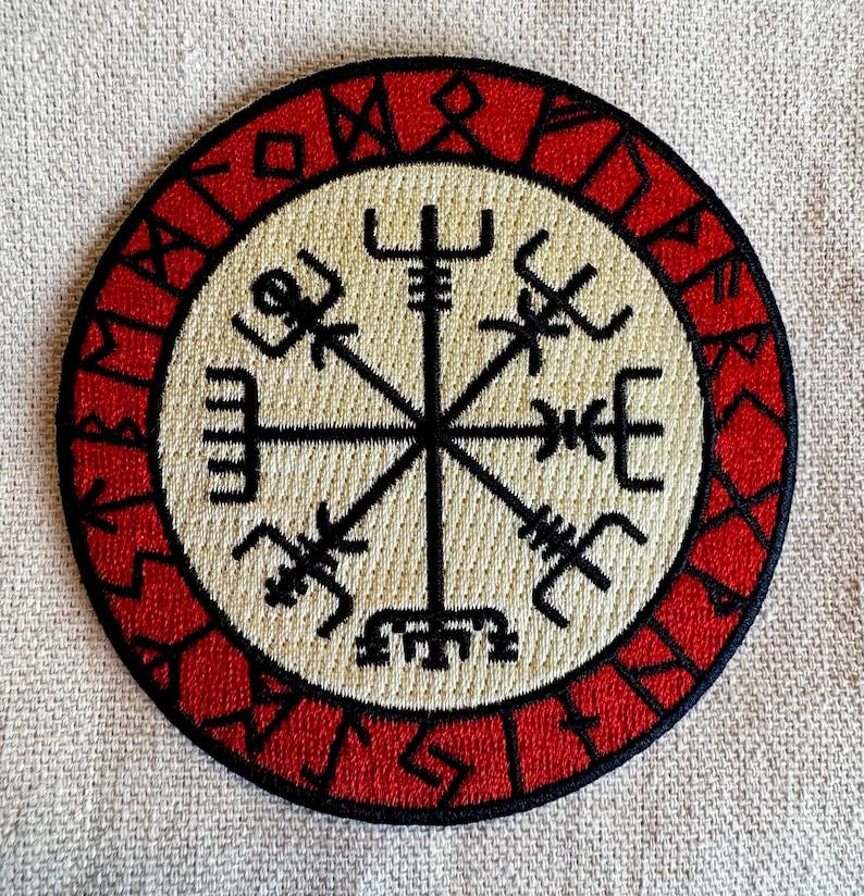 May include: A red and white embroidered patch with a black compass design. The compass has eight points and is surrounded by a circle of runes.