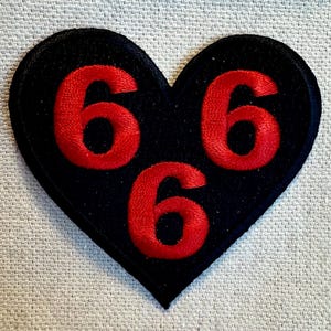 May include: A black heart-shaped patch with three red embroidered numbers "666" on it.