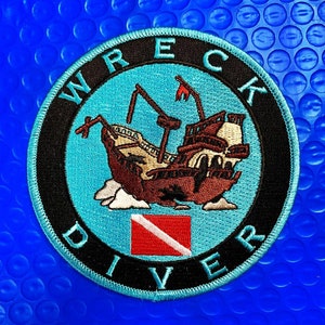 May include: A blue and black embroidered patch with the words "Wreck Diver" and a depiction of a sunken ship with a scuba diving flag.