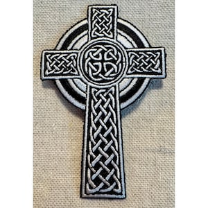 May include: A black and white embroidered Celtic cross patch with a circular design. The cross is made of intricate knotwork and the circle has concentric rings.