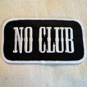 Peut inclure: Écusson brodé noir et blanc avec des coutures blanches autour des bords. L'écusson dit "NO CLUB" en lettres blanches.