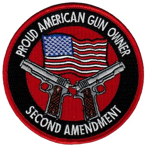 May include: A red, white, and blue American flag with two crossed silver pistols. The flag is surrounded by a black circle with the text "Proud American Gun Owner Second Amendment" in white.