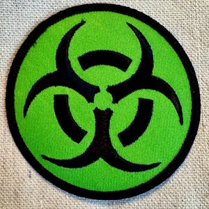 May include: A green and black biohazard symbol patch. The symbol is a stylized three-pronged shape with a black outline and a green background.
