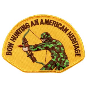 Op de afbeelding: Een geborduurd geel patch met een bruine rand. De patch toont een persoon in camouflagekleding die een boog en pijl vasthoudt. De tekst "Bow Hunting An American Heritage" is geschreven in een bruine cirkelboog rond de persoon.