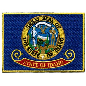 May include: Embroidered patch featuring the state seal of Idaho. The seal is a gold circle with the words "Great Seal of the State of Idaho" around the edge. Inside the circle is a depiction of a mountain range, a sun, and a farmer holding a plow. Below the seal is a red ribbon with the words "State of Idaho" in gold lettering.
