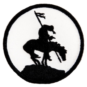 May include: A circular patch featuring a black silhouette of a rider on a horse, holding a flag. The design is set against a white background, framed by a black border. The patch is likely an emblem or insignia.