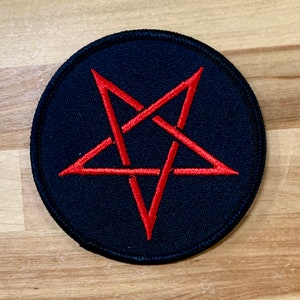 May include: A black and red embroidered patch with a pentagram design. The pentagram is red and the background is black.