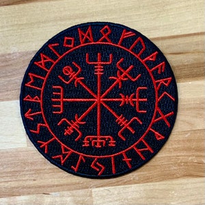 Op de afbeelding: Een geborduurde zwarte en rode patch met een kompasontwerp en de tekst "Vegvisir" in runen rond de rand.