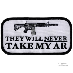 Puede incluir: Parche blanco bordado con contorno negro. El parche presenta una silueta negra y gris de un rifle de asalto con el texto "They Will Never Take My AR" en negro.