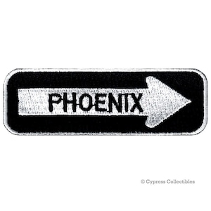 May include: Black and white embroidered patch with a white arrow pointing to the right and the word "PHOENIX" in white letters.