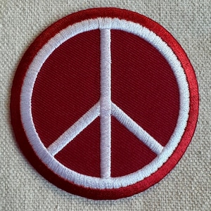May include: A red embroidered peace sign patch with a white outline. The patch is circular and has a satin finish.
