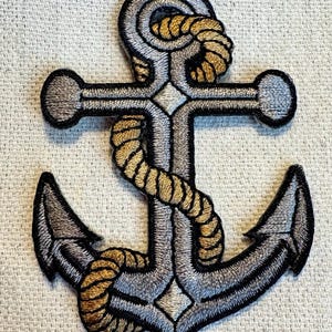 May include: A silver anchor with a gold rope wrapped around it. The anchor is embroidered and has a detailed design.