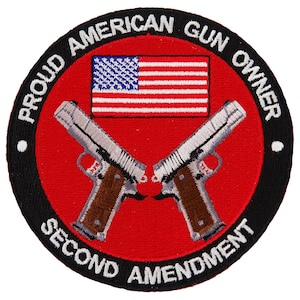 Puede incluir: Un parche bordado negro y rojo con el texto "Proud American Gun Owner Second Amendment" y un par de pistolas plateadas cruzadas. La bandera estadounidense está en el centro del parche.