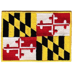 May include: An embroidered patch of the Maryland state flag. The flag features a black and gold checkered pattern with a red and white crest in the center.