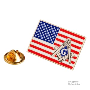 Op de afbeelding: Een gouden reversbadge met een kleine Amerikaanse vlag waarop een blauw en gouden vrijmetselaarsymbool is gelegd.