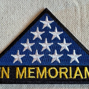 May include: A blue triangular patch with white stars and the text "IN MEMORIAM" in gold lettering on a black background.