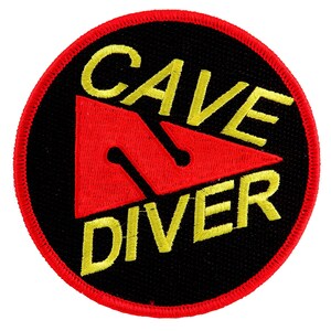 Puede incluir: Un parche bordado negro y rojo con el texto "Cave Diver" en letras amarillas. El parche presenta un triángulo rojo con un contorno amarillo.