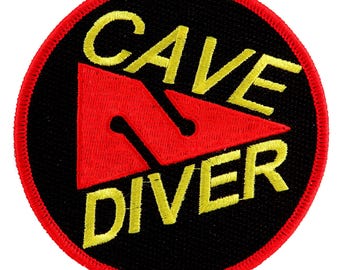 Könnte beinhalten: Ein gestickter schwarzer und roter Aufnäher mit dem Text "Cave Diver" in gelben Buchstaben. Der Aufnäher zeigt ein rotes Dreieck mit gelbem Umriss.