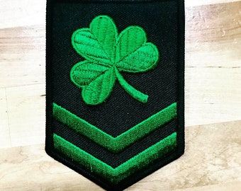 May include: A black and green embroidered patch with a four-leaf clover and two green chevron stripes.