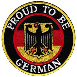 May include: A round embroidered patch with a black background and a yellow border. The center of the patch features a black eagle with red talons and a yellow beak, standing on a red, yellow, and black German flag. The text "Proud to be German" is written in white around the outside of the patch.