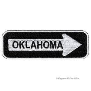 Könnte beinhalten: Schwarzer und weißer gestickter Aufnäher mit einem weißen Pfeil, der nach rechts zeigt, und dem Wort "OKLAHOMA" in Schwarz.