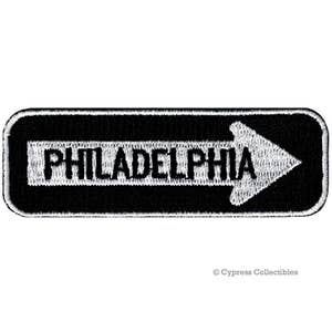 May include: Black and white embroidered patch with a white arrow pointing to the right and the word "PHILADELPHIA" in white letters.