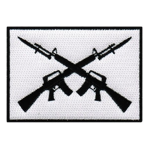 Könnte beinhalten: Ein weißer Patch mit einem schwarzen gestickten Design aus zwei gekreuzten Gewehren.