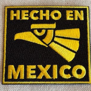 Puede incluir: Parche bordado negro con puntadas amarillas. El parche presenta el texto "HECHO EN MEXICO" y un diseño de águila estilizado.