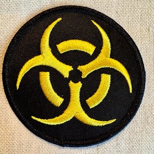 May include: A yellow biohazard symbol embroidered on a black circular patch.